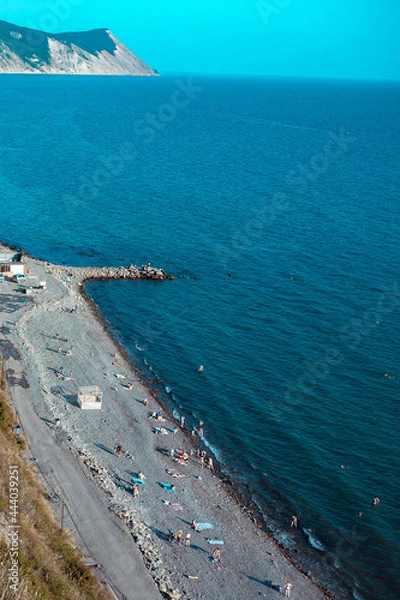 Fototapeta Vacationing tourists on the stone coast of a beautiful sea. A crowd of people resting on the beach near the blue sea.