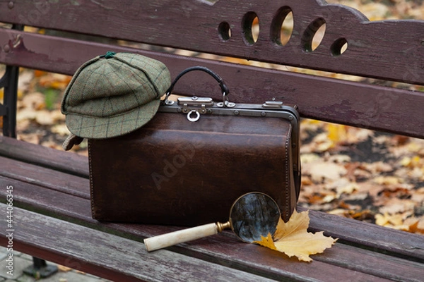 Obraz Travel bag and large magnifying glass stands on wooden bench