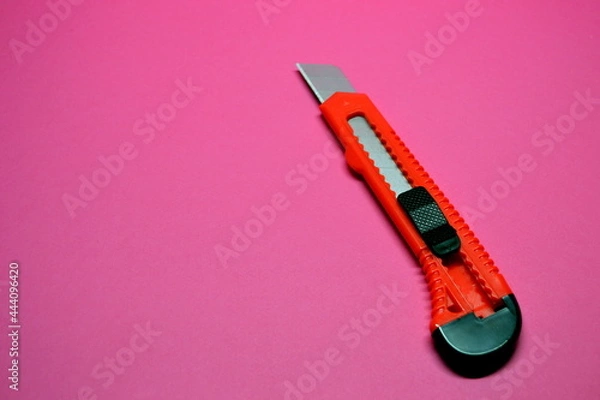 Obraz Red cutter knife on red background, sharp knife stationery