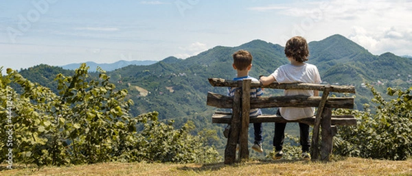 Fototapeta Two little brothers sitting on the bench and watching the long big mountains with forest, thinking, young, life