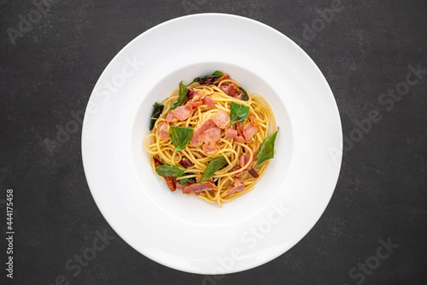 Fototapeta top view shot of Spaghetti Pasta with Dried Chilli, Garlic, Sweet Basil and Bacon in white ceramic plate on dark tone texture background