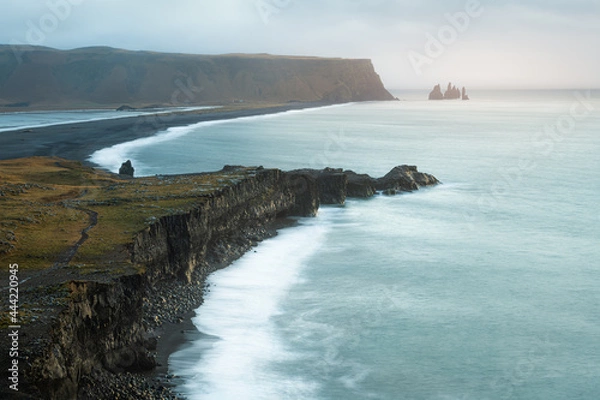 Fototapeta Dramatic stormy sunrise with clouds, fog and sunshine at scenic Kirkjufjara cliff looking to Reynisfjara black sand beach and Reynisdrangar in Iceland