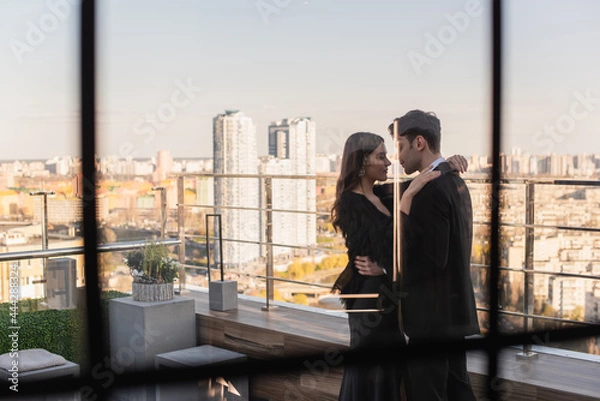 Fototapeta side view of couple hugging on terrace behind blurred window of restaurant