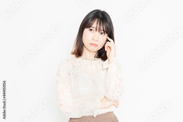 Fototapeta 白背景の前に立って、悩んでいる、レースのブラウスを着た若い女性