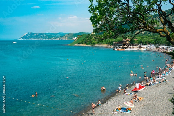 Fototapeta Beautiful coast of the Black Sea with a crowd of tourists on a background of green hills. The beach with many tourists resting in the sun with hot weather.