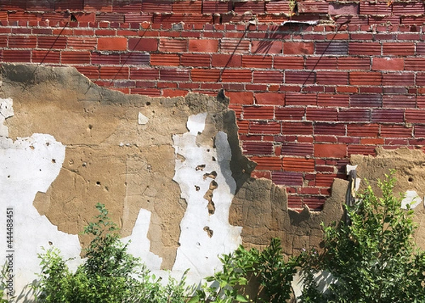 Obraz Weathered cement plaster peeling back to expose old red brick wall of abandoned building in American Midwest.