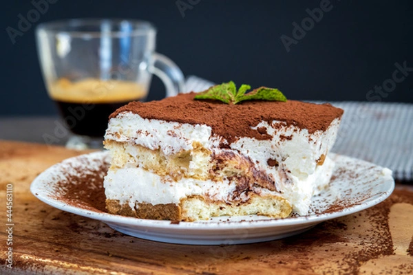 Obraz Slice of eaten traditional tiramisu cake with a cup of coffee in the background. Authentic gluten-free Italian layered dessert with ladyfinger biscuits, mascarpone cheese cream and cocoa powder. Side