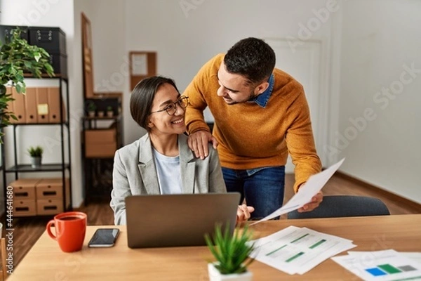 Fototapeta Two business workers smiling happy working sitting on desk at the office.