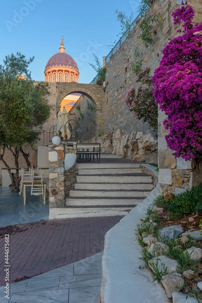 Fototapeta  Scenic view of stairs leading to st nikolas church with a blooming bougainvillea aside and an extrerior of a traditional cafe , in ermoupolis Syros Greece