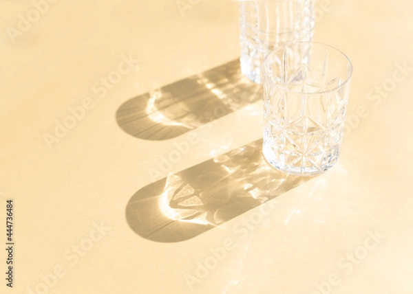 Fototapeta Two glasses on the gold background or yellow background in natural sunlight with shadows. Minimalist creative composition.