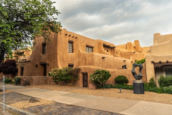Fototapeta Pueblo Revival Style building with earth tone color, rounded corners and battered walls under dramatic cloudy sky, side, New Mexico Museum of Art, Santa Fe, New Mexico