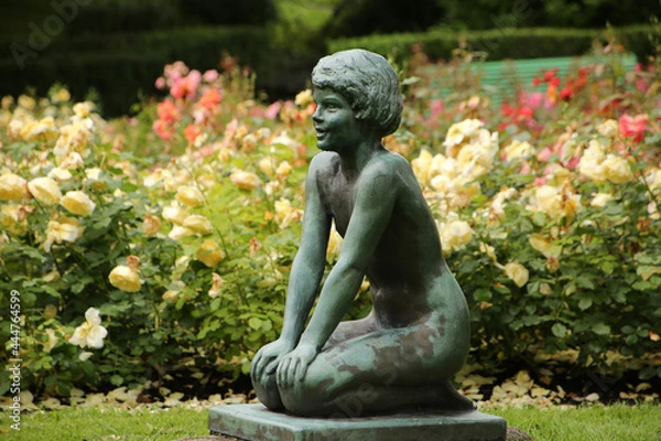 Obraz Small sculpture or statue of a little girl kneeling surrounded by plants and trees in the center of the Byparken, which is a pretty public park in the center of the city of Haugesund, Norway.