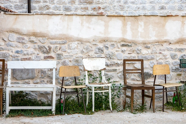 Fototapeta Row of vintage wooden chairs in front of an old stone building, lined up next to a petanque field for players to rest.