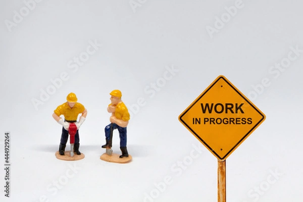 Obraz Small figure workers on white background with message Work In Progress 