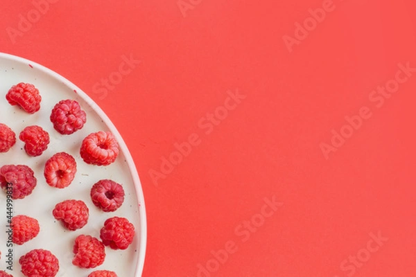 Fototapeta Ripe raspberry fruits on plate, healthy pile of summer berries  top view. Pattern flat lay of red scarlet  raspberry on pink background with free copy space for text