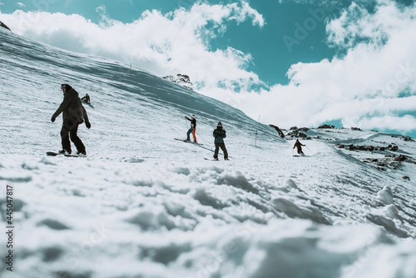 Fototapeta People in winter enjoying the snowy mountains where are practised plenty of activities such as skiing and snowboarding with a clear sky and some clouds on the horizon.