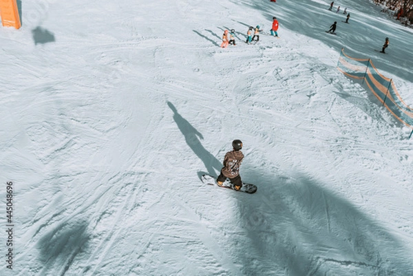 Fototapeta People in winter enjoying the snowy mountains where are practised plenty of activities such as skiing and snowboarding with a clear sky and some clouds on the horizon.