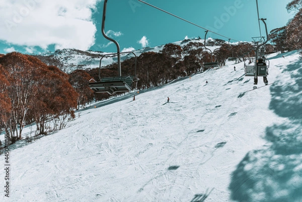 Fototapeta People in winter enjoying the snowy mountains where are practised plenty of activities such as skiing and snowboarding with a clear sky and some clouds on the horizon.