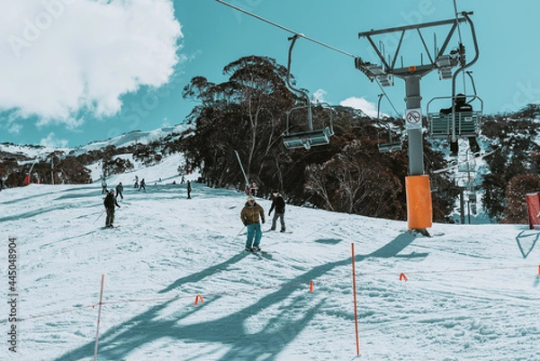 Fototapeta People in winter enjoying the snowy mountains where are practised plenty of activities such as skiing and snowboarding with a clear sky and some clouds on the horizon.