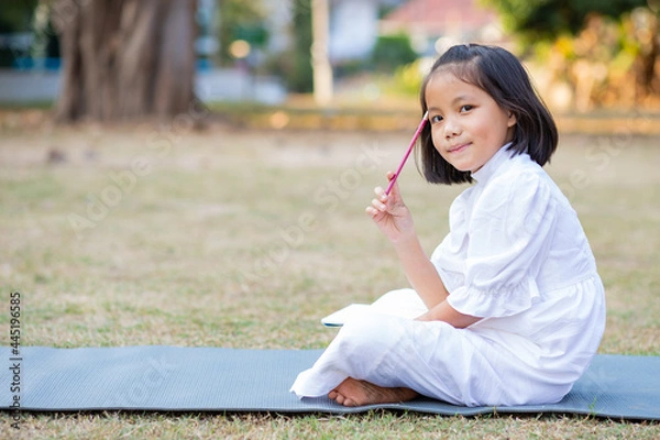 Fototapeta Little adorable Asian kid lying down on mat writing on notebook, Concept of outdoor education, A girl doing her homework, Kid like reading book