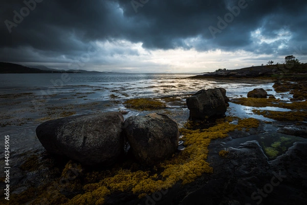 Fototapeta Fjord landscape with rocks in the foreground and dramatic cloudy sky in northern norway during sunset