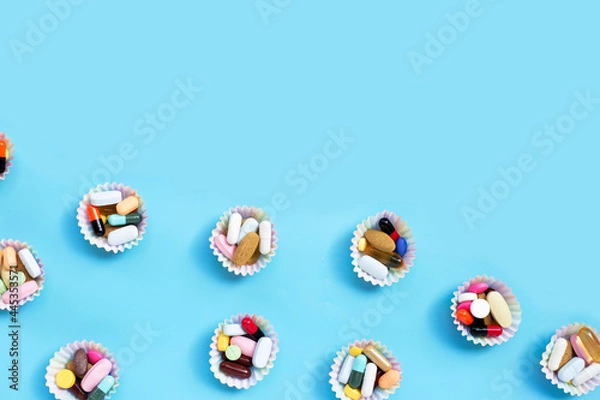 Fototapeta Colorful tablets with capsules and pills in cupcake wrappers on blue background.