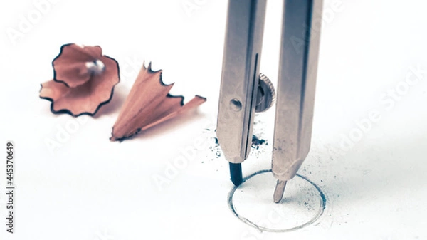Fototapeta Macro detail closeup of a school geometry drawing compass drafting a round circle on white student paper with study pencil shavings in the background, with copyspace