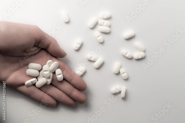 Obraz Hand holding many dosages of chemical opioids medical pills and a pile of pharmaceutical medication on clean white background with copyspace - Concept of abuse addiction, antibiotic or healthcare