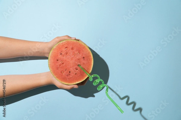 Obraz Hand holding half watermelon with straw on a pastel blue background with copy space minimal