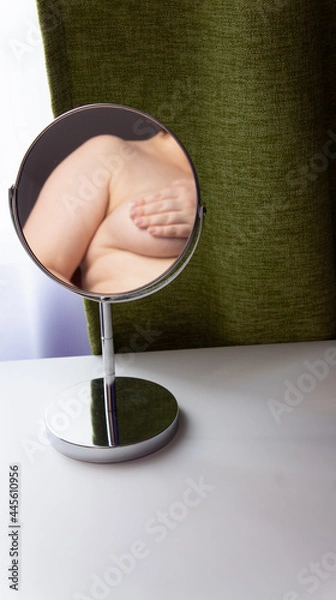 Fototapeta Figure of a fat woman is reflected in a round mirror. Mirror stands on a white table on green curtains background
