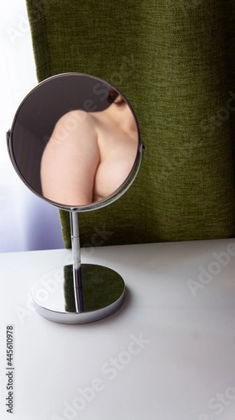 Fototapeta Figure of a fat woman is reflected in a round mirror. Mirror stands on a white table on green curtains background