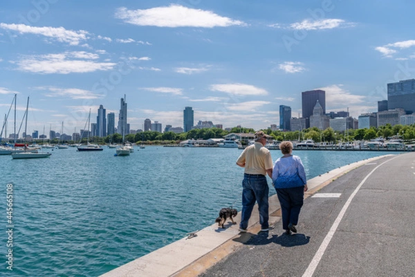 Obraz A senior couple enjoys a walk with their dog in Chicago, along the Lakefront Trail, on a lovely summer day.