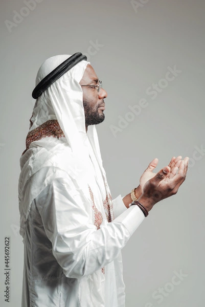 Obraz Photo from the side. Arab man in white clothes praying in the mosque stretching out his hands with palms up