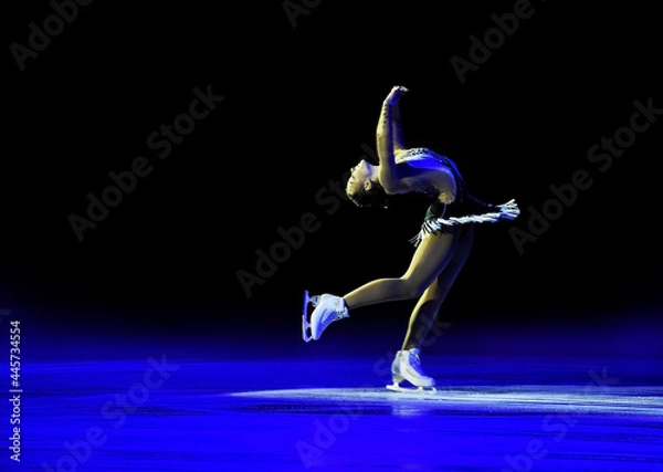 Fototapeta Reclined spin performed by a professional ice skater with artistic blue light and black background