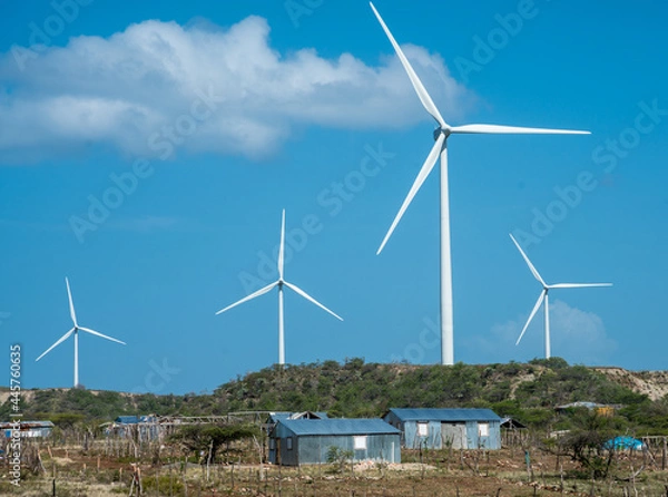 Fototapeta Dramatic image of wind turbines in the wind, with small poor Caribbean village in foreground.