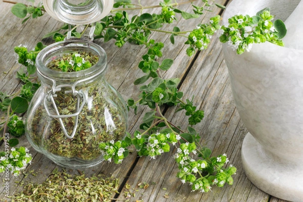 Fototapeta Dried Oregano on a jar over a wooden table with mortar and branches with flowers around it