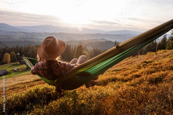Fototapeta Woman hiker resting after climbing in a hammock at sunset