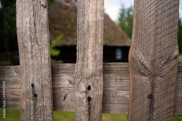 Fototapeta Rails of a rural wooden fence with a hut in the background.