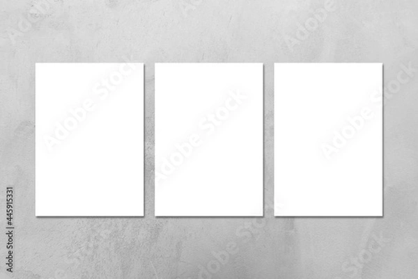 Fototapeta Three empty white vertical DIN A4 rectangle poster or business card mockups on the gray concrete stone wall.Flat lay, top view. For advertising, brand design, stationery presentation.