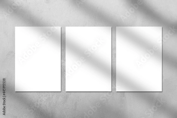Fototapeta Three empty white vertical rectangle poster or business card mockups with window shadow on the gray concrete stone wall. Flat lay, top view. For advertising, brand design, stationery presentation.