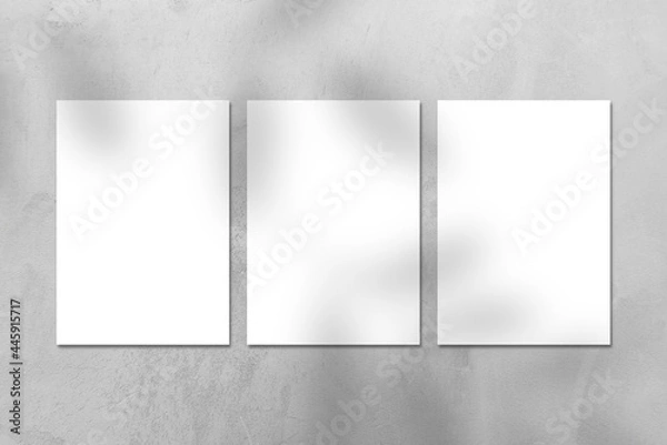 Fototapeta Three empty white vertical A4 rectangle poster or business card mockups with tree leaves shadow on gray concrete stone wall. Flat lay, top view. For advertising, brand design, stationery presentation.