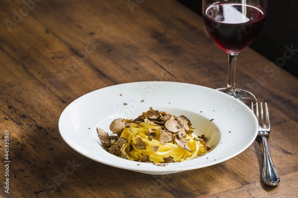 Obraz Pasta with truffles and glass of red wine on wooden table copy space.	