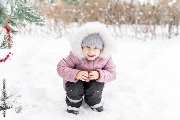 Fototapeta playful little girl with christmas ball by a snowy spruce on a winter day