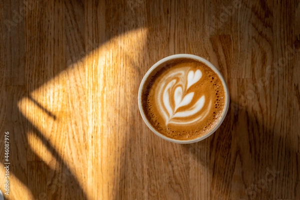 Fototapeta Cup of coffee with latte art on wooden table. Fresh cappuccino on wooden background. Coffee break. Morning coffee with milk. Sun and shadow. Top view, flat lay, copy space. 