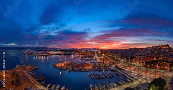 Fototapeta Cagliari, Italy 12-06-2021. Panoramic view of Cagliari at sunset view of the harbor. Cagliari at night seen from above.  Amazing view of Cagliari city with ships and boats moored at the port.
