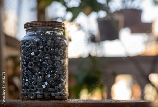 Fototapeta glass jar full of screw nuts with blurred background. copy space