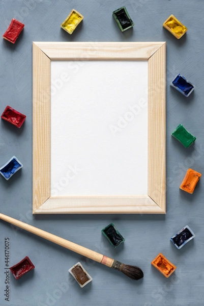 Obraz Stationery mock-up scene. Blank white greeting card in wooden frame surrounded bywatercolor paints in ditches and a round squirrel brush on textured gray background.