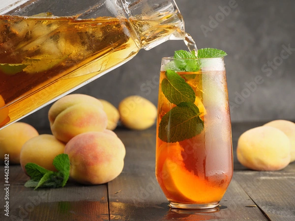 Fototapeta Peach ice tea with mint and ice on a dark wooden background.