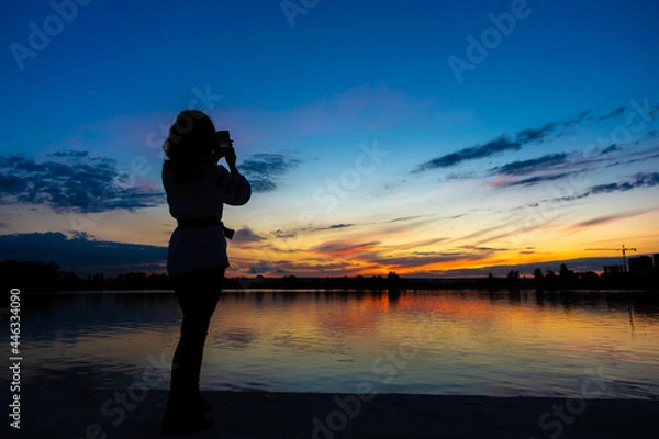 Fototapeta Silhouette of a girl with a phone on the background of sunset by the lake