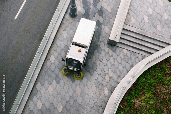 Fototapeta Special machine cleans the city street from dirt. A sweeper with round brushes washes the paving slabs. The concept of clean streets from garbage. View from above